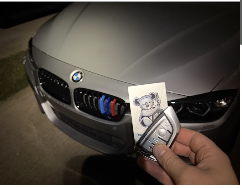 BMW key fob and Koala Locksmith card held in front of the silver BMW 320i